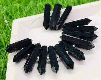 May include: A collection of black gemstone beads in a pointed, faceted shape. The beads are strung on a silver wire and are arranged in a circular pattern.
