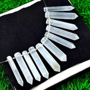 Puede incluir: Un collar de cuentas de cristal transparentes y alargadas, con extremos puntiagudos. Las cuentas están ensartadas en un fino hilo plateado, sobre un fondo negro. Los cristales tienen un aspecto translúcido, ideal para joyería.