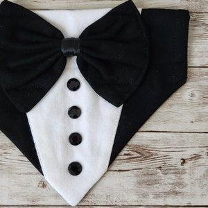 May include: A black and white tuxedo-style dog bandana with a black bow tie and four black buttons.
