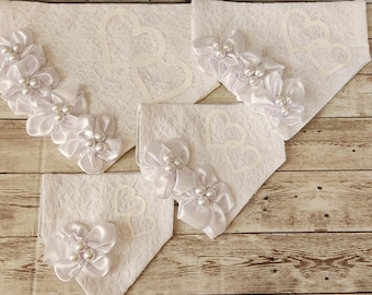 May include: Four white lace dog bandanas with pearl embellishments and white satin bows. The bandanas have a heart design.
