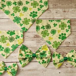 Puede incluir: Un conjunto de cuatro bandanas para perros verdes y amarillas con un patrón de trébol y huella de pata, y dos pajaritas a juego.