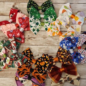 May include: A collection of 12 colorful fabric bow ties with various patterns, including plaid, polka dots, and floral designs. The bow ties are arranged in a circle on a wooden surface.