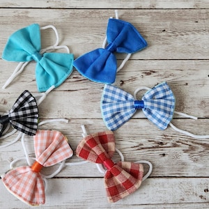 May include: Six fabric bow ties in various colors and patterns, including blue, red, black, and white, on a light wood background.
