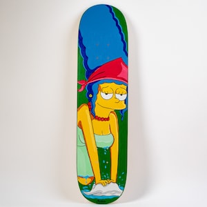 K&ouml;nnte beinhalten: Ein gr&uuml;nes Skateboard-Deck mit einer Cartoon-Illustration von Marge Simpson, die ein rotes Bandana und ein gr&uuml;nes Kleid tr&auml;gt. Sie w&auml;scht ihre H&auml;nde in einem blauen Waschbecken mit wei&szlig;en Blasen.