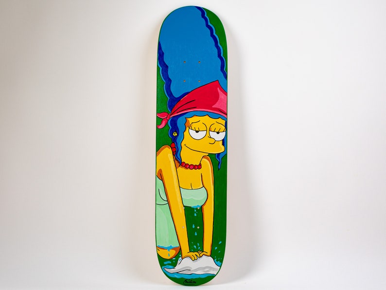 K&ouml;nnte beinhalten: Ein gr&uuml;nes Skateboard-Deck mit einer Cartoon-Illustration von Marge Simpson, die ein rotes Bandana und ein gr&uuml;nes Kleid tr&auml;gt. Sie w&auml;scht ihre H&auml;nde in einem blauen Waschbecken mit wei&szlig;en Blasen.