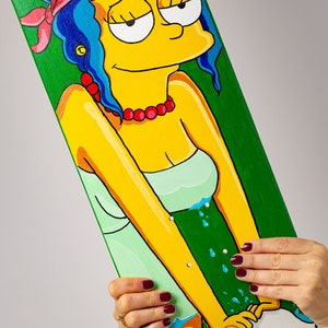 K&ouml;nnte beinhalten: Ein gr&uuml;nes Skateboard-Deck mit einem handgemalten Bild eines gelben Comic-Charakters mit blauen Haaren, der ein rotes Bandana und ein gr&uuml;nes Kleid tr&auml;gt. Der Charakter ist beim H&auml;ndewaschen in einem wei&szlig;en Waschbecken mit blauem Wasser dargestellt.