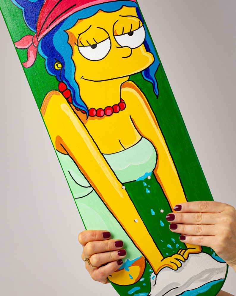 K&ouml;nnte beinhalten: Ein gr&uuml;nes Skateboard-Deck mit einem handgemalten Bild eines gelben Comic-Charakters mit blauen Haaren, der ein rotes Bandana und ein gr&uuml;nes Kleid tr&auml;gt. Der Charakter ist beim H&auml;ndewaschen in einem wei&szlig;en Waschbecken mit blauem Wasser dargestellt.