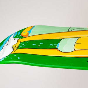 K&ouml;nnte beinhalten: Ein gr&uuml;nes Skateboard-Deck mit einem bemalten Design einer Person mit gelben Beinen und einem gr&uuml;n-wei&szlig;en Badeanzug. Die Person steht im Wasser mit einer wei&szlig;en Welle dahinter. Das Deck ist mit blauen und wei&szlig;en Wassertropfen bemalt.