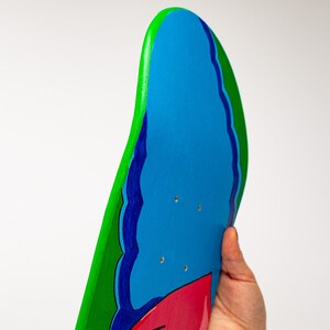 K&ouml;nnte beinhalten: Ein blaues, gr&uuml;nes und rotes Skateboard-Deck mit einem wellenf&ouml;rmigen Design. Das Deck ist aus Holz und hat eine glatte Oberfl&auml;che.