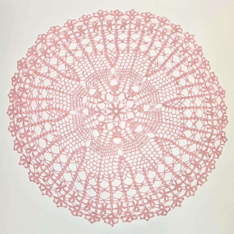 Puede incluir: Un delicado encaje de ganchillo rosa con un dise&ntilde;o circular. El encaje tiene un centro con un patr&oacute;n floral y un intrincado encaje alrededor de los bordes.