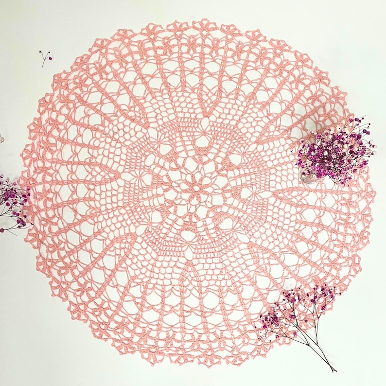 Puede incluir: Un delicado encaje de ganchillo rosa con un dise&ntilde;o circular. El encaje tiene un centro con un patr&oacute;n floral y un trabajo de encaje intrincado.
