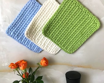 Puede incluir: Tres agarraderas de olla de ganchillo en azul, blanco y verde. Las agarraderas de olla son de forma cuadrada y tienen un asa de bucle.