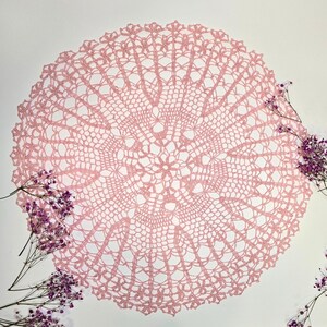 Puede incluir: Un delicado encaje de ganchillo rosa con un dise&ntilde;o circular. El encaje tiene un patr&oacute;n intrincado con un motivo floral central.