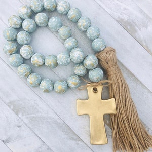 May include: A light blue and gold beaded garland with a gold cross charm and a brown tassel.