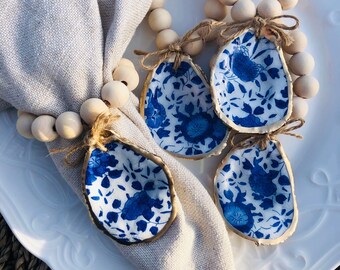 May include: A set of four blue and white oyster shell napkin rings with gold trim. The rings are attached to a wooden bead garland.