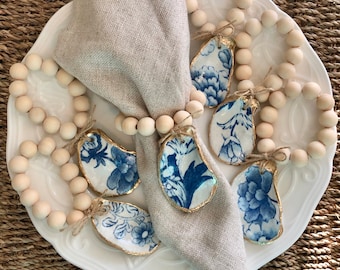 May include: A set of blue and white oyster shell napkin rings with gold accents. The rings are strung on a wooden bead garland.