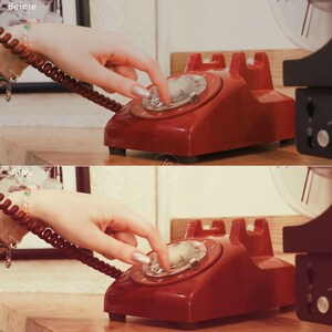 Puede incluir: Un tel&eacute;fono rojo vintage con dial giratorio y dial transparente. El tel&eacute;fono est&aacute; sobre una superficie de madera. La imagen muestra el tel&eacute;fono en uso.
