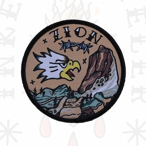 Puede incluir: Un parche redondo de color beige con un borde negro. El parche presenta un águila de dibujos animados con una valla de alambre de púas y la palabra "LION" encima. El águila está volando sobre una cordillera con un río que la atraviesa. El parche es para artículos de exterior.