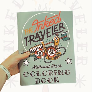 Puede incluir: Un libro para colorear de color verde azulado titulado "The Inked Traveler" con una ilustración con temática de tatuajes. La portada presenta una máquina de tatuar, flores y estrellas. El libro está etiquetado como "National Park Coloring Book".