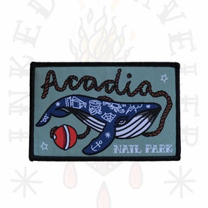 May include: A rectangular patch with a blue whale design. The patch features the word "Acadia" in a rope-style font, a red buoy, and the words "NAIL PARK". The whale is blue with white stripes.