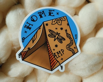 May include: A blue and brown sticker with a tent design and the text "HOME + CAMP" in a vintage style font.