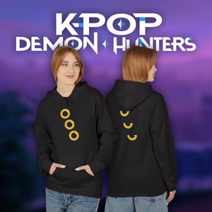 May include: Black hoodie with a front pocket and drawstring hood. The front features three yellow circles, and the back has three yellow crescent shapes. The text "K-POP DEMON HUNTERS" is displayed in white and blue.