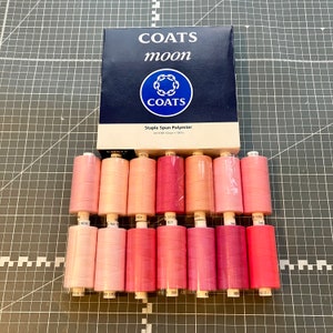 May include: A box of Coats Moon Staple Spun Polyester thread in a variety of pink shades. The box is blue with white lettering and a logo. There are 12 spools of thread in the image.