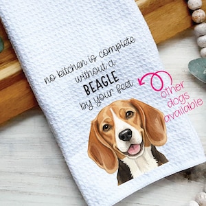 May include: White kitchen towel with a beagle dog graphic. The towel has the text "no kitchen is complete without a BEAGLE by your feet." The beagle has brown and white fur and is smiling. Other dog breeds are available.