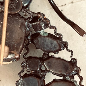 K&ouml;nnte beinhalten: Nahaufnahme der R&uuml;ckseite einer Vintage-Brosche. Die Brosche ist aus Metall und hat ein kettenartiges Design. Die R&uuml;ckseite der Brosche hat eine Nadel und einen Metallverschluss.