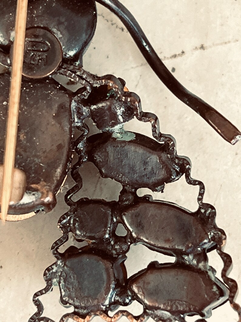 K&ouml;nnte beinhalten: Nahaufnahme der R&uuml;ckseite einer Vintage-Brosche. Die Brosche ist aus Metall und hat ein kettenartiges Design. Die R&uuml;ckseite der Brosche hat eine Nadel und einen Metallverschluss.