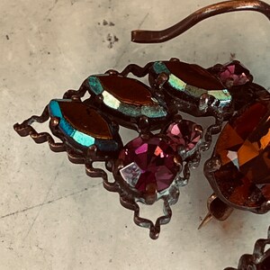 K&ouml;nnte beinhalten: Eine Vintage-Brosche mit einem dekorativen Design aus schillernden blauen und violetten Glassteinen und einer goldfarbenen Metallnadel.