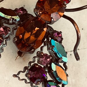 K&ouml;nnte beinhalten: Eine Vintage-Brosche in Form eines stilisierten Schmetterlings mit schillernden und braunen Strasssteinen. Die Brosche ist aus Metall und hat eine Nadel.