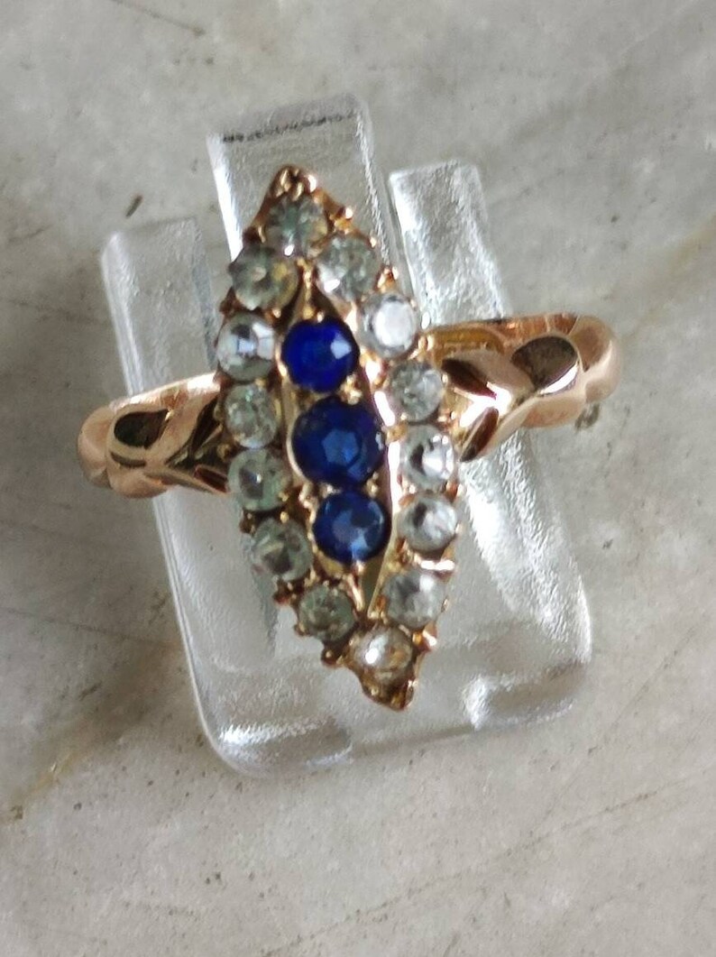 May include: A gold ring with a marquise-shaped setting featuring three blue sapphires surrounded by smaller clear stones.