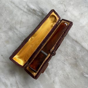 May include: A brown leather case with a gold lining, open to reveal a brown and white cigarette holder.