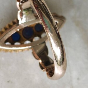 May include: A gold ring with a blue and white stone setting. The ring is set with three blue stones and a row of white stones around the edge.