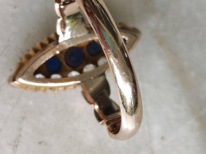 May include: A gold ring with a blue and white stone setting. The ring is set with three blue stones and a row of white stones around the edge.