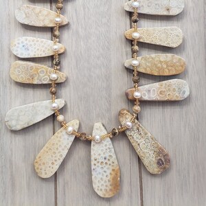 May include: A necklace made with fossilized coral and pearl beads. The coral pieces are teardrop shaped and have a light brown color. The necklace has a gold clasp and a tag that reads "Works of Love by Cynthia".