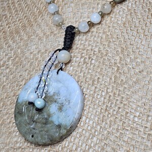 May include: A necklace with a large, round, green and white jade pendant. The pendant is attached to a black cord with clear crystal beads. The necklace is made of white and brown beads.