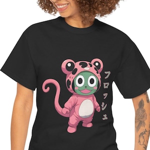 Peut inclure: T-shirt noir avec un personnage de dessin animé portant un costume de grenouille rose et blanc. Le personnage a la peau verte et une longue queue. Le texte japonais sur le t-shirt est "FROGUSH", qui est le nom du personnage.