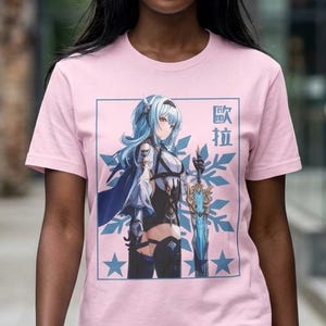 May include: A light pink t-shirt featuring a graphic of a female anime character with blue hair and a sword. The graphic is framed in a blue rectangle with stars and Japanese text. The shirt is being worn.