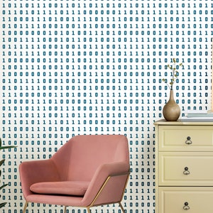 May include: A pink velvet armchair with gold metal legs sits in front of a white wall with a blue and white binary code pattern wallpaper. A dresser with three drawers and a vase with a dried plant are on the right side of the image.