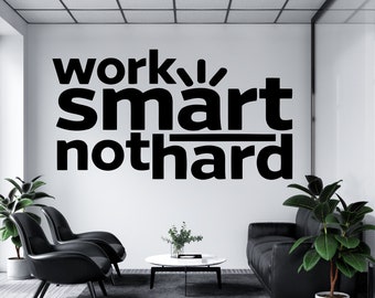 Może przedstawiać: Biała ściana z czarnym tekstem, który brzmi "work smart not hard" w nowoczesnym biurowym otoczeniu. W pomieszczeniu znajdują się dwa czarne krzesła i czarna sofa, a także dwie doniczkowe rośliny.