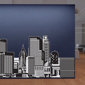 May include: Black and white silhouette of a city skyline with tall buildings, including a dome-shaped building in the centre. The skyline is on a blue wall.