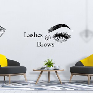 Può includere: Un muro bianco con il testo "Lashes & Brows" e un'illustrazione in bianco e nero di un occhio con ciglia lunghe e un sopracciglio. Due sedie gialle e grigie sono di fronte a un tavolino da caffè in legno con una pianta in vaso e una tazza sopra.