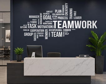 Puede incluir: Una pared azul oscuro con un gran vinilo decorativo blanco que presenta un diseño de nube de palabras centrado en el término TEAMWORK. Las palabras circundantes incluyen GOAL, TASK, PLAN, PROCESS, LEADER y COOPERATION. Debajo hay un mostrador de mármol blanco.