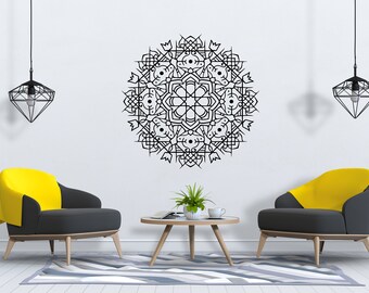 May include: Two black and yellow armchairs with wooden legs face each other in a living room setting. A coffee table with a book and a cup sits between the chairs. A black geometric pendant light hangs from the ceiling above each chair. A large black mandala design is on the white wall behind the chairs.