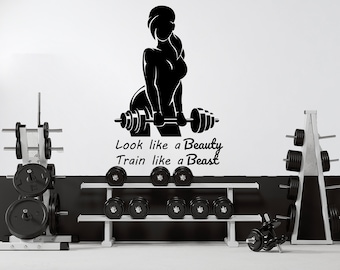 May include: Black and white silhouette of a person lifting weights with the text "Look like a Beauty Train like a Beast". The image is set against a white wall with two weight racks in the background.