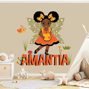 May include: A wall decal featuring a cartoon fairy with black hair and yellow bows, wearing an orange dress and apron. The name "AMANTIA" is displayed in orange letters. A butterfly and other decorative elements complete the design, suitable for a child's room.