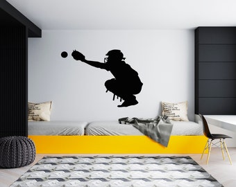 May include: Black silhouette of a baseball catcher in a catching position with a ball in the air. The silhouette is on a white wall in a room with a yellow bed and a black chair.