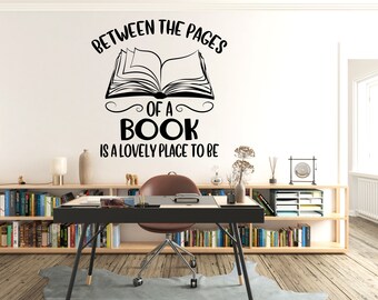 Puede incluir: Pegatina de pared en blanco y negro con el texto "Between the pages of a book is a lovely place to be" y una imagen estilizada de un libro abierto.